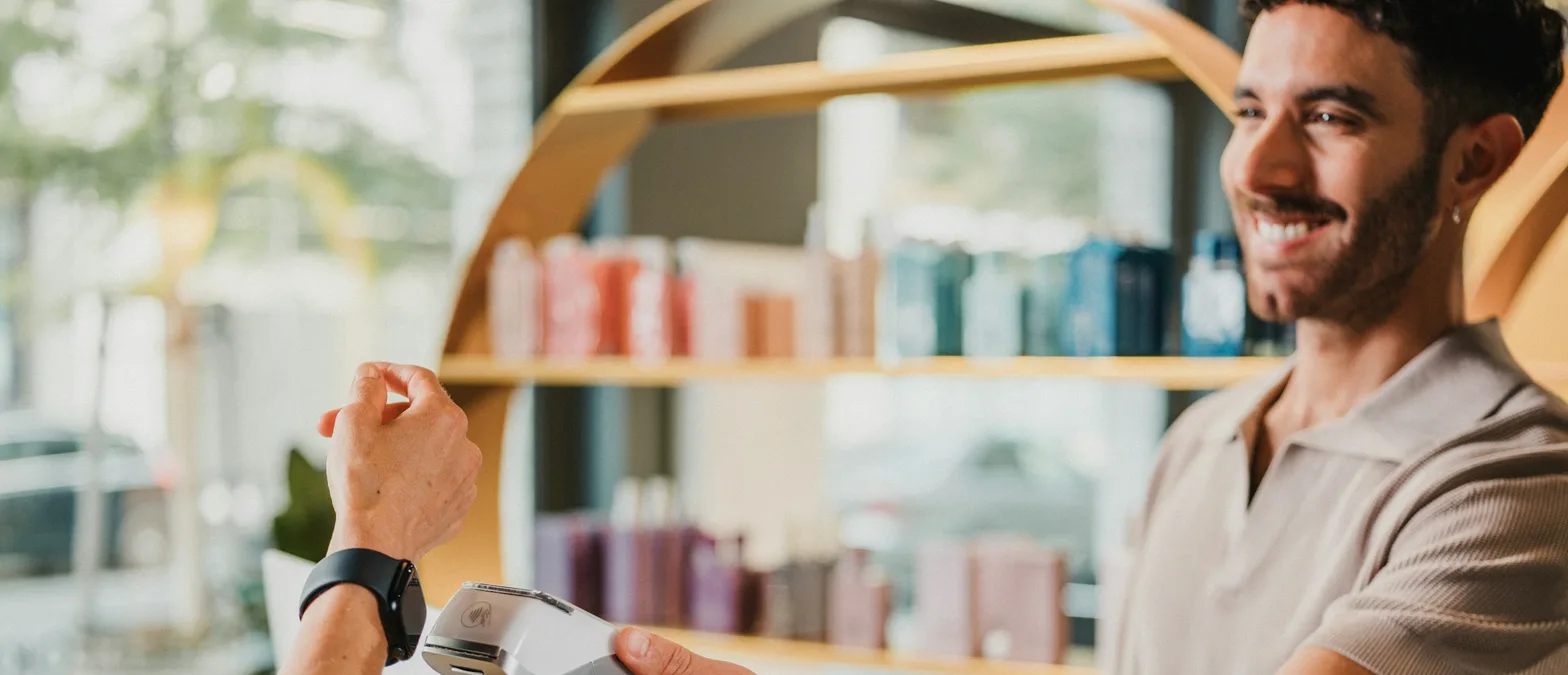 A customer tapping a payment terminal held out by a smiling shop employee at a retail counter, a stand-in for the moment a deposit changes hands on a special order.